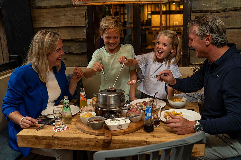 Twee kinderen en hun ouders genieten van een fondue maaltijd