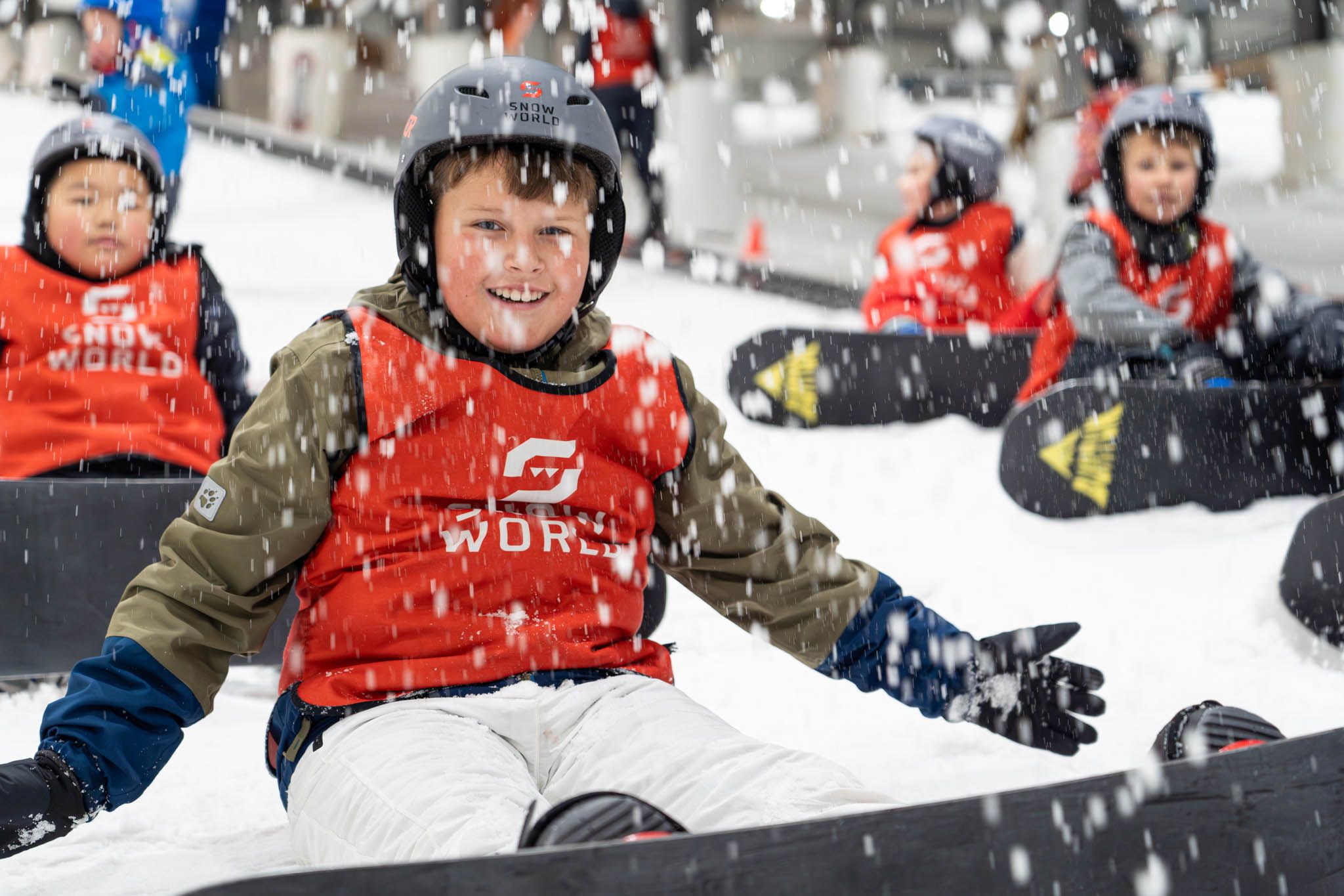 Een groep kinderen met snowboards die plezier hebben zittend in de sneeuw op een piste