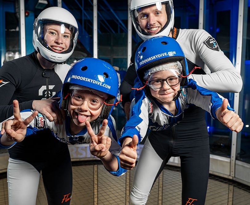 Twee kinderen poseren met ouders met skydiving uitrusting aan